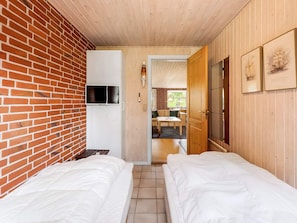 Ein Zimmer mit zwei Betten, einem an einer Ziegelwand befestigten Fernseher und Holzvertäfelung.