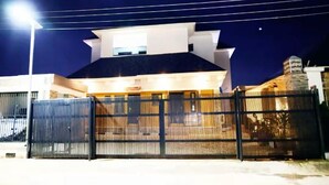 Een omheind landgoed bij nacht met een modern architectonisch ontwerp, een opvallend dak en een goed verlichte entree.