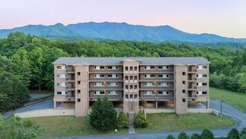 A multi-story hotel with a central entrance, surrounded by lush greenery and mountains in the background.