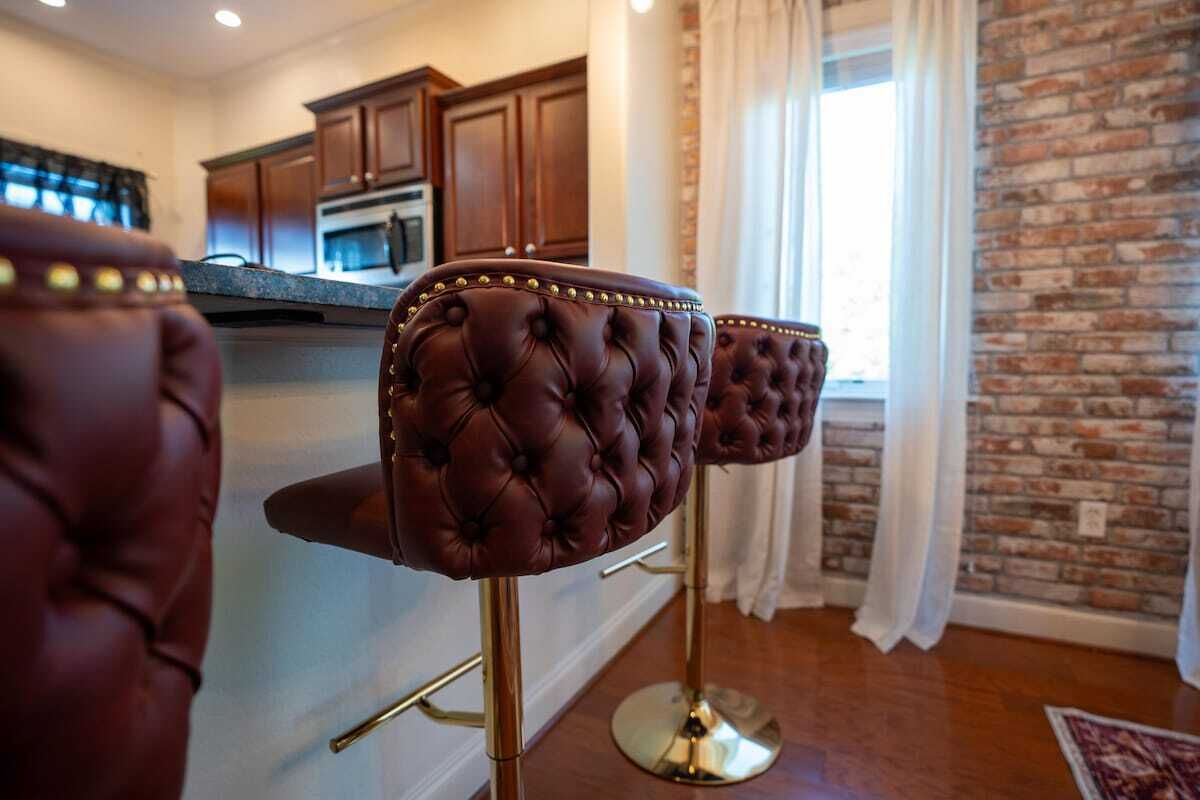 A kitchen area with dark brown bar stools, a stainless steel refrigerator, and wooden cabinets.