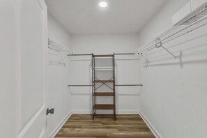Ein begehbarer Kleiderschrank mit einem zentralen Holzladderschrank, Metallregalen an den Wänden und einem Holzboden.