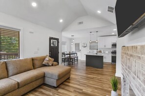 Ein modernes Wohnzimmer mit Ecksofa, Essbereich und Küche mit weißen Schränken.