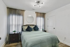 Ein Schlafzimmer mit einem Bett, Nachttischen, einem Spiegel und einer Deckenleuchte.