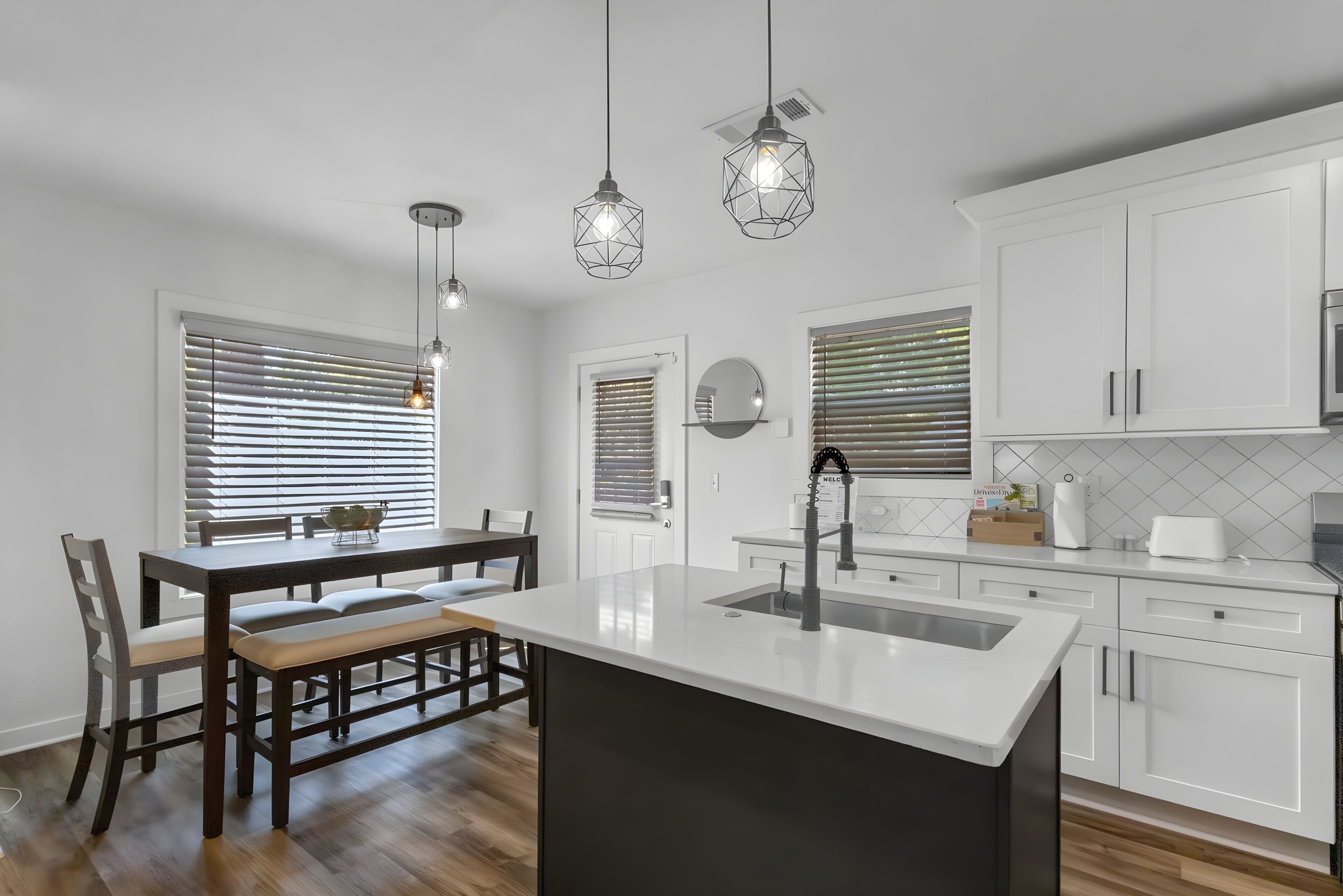 Een moderne keuken met witte kasten, een centraal eiland, hanglampen en een eetgedeelte met een bank.