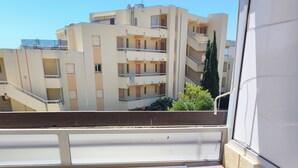 En balkon med et hvidt bord, en hvid stol, flisegulv og udsigt til høje bygninger.