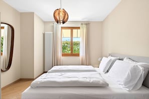 Ein Schlafzimmer mit Bett, einem fenster mit Vorhängen, einem Heizkörper und einer Pendelleuchte.