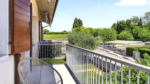 Ein Balkon mit Stuhl, Blick auf einen Park und ein Gebäude mit Holzfassade.