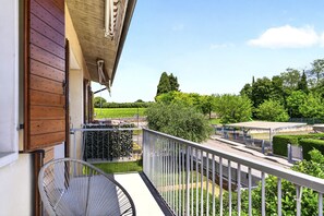 A balcony with a chair, a view of a park, and a building with a wooden facade.