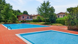 Ein Schwimmbeckenbereich mit zwei Pools, umgeben von Grünflächen und Wohnhäusern.