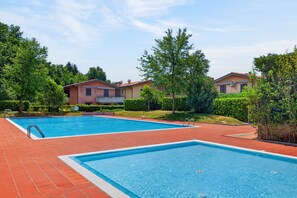 A swimming pool area with two pools, surrounded by greenery and residential buildings.