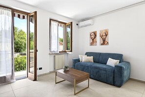 A living room with a sofa, a coffee table, a sliding glass door, and two wall art pieces.