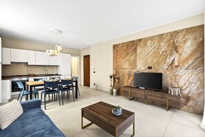A modern living room with a sofa, coffee table, TV, and a dining area with chairs and a table.
