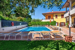Ein Schwimmbecken mit Liegestühlen, einem umzäunten Bereich und einem Gebäude mit Balkonen.