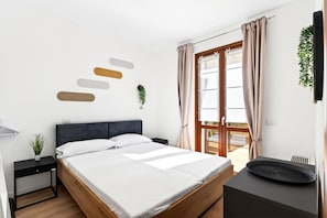 Ein modernes Schlafzimmer mit einem Bett, Nachttischen, einer Pflanze und Blick ins Freie.
