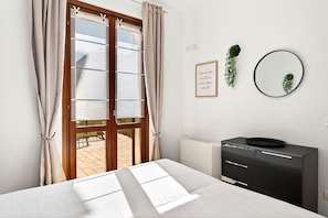 Ein Schlafzimmer mit einem Bett, einem Schminktisch, einem Fenster mit Vorhängen, einer Heizung und einem an der Wand befestigten Spiegel.