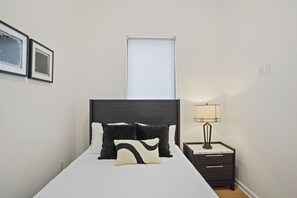 A neatly made bed with a dark headboard, a bedside lamp, and a framed picture on the wall.