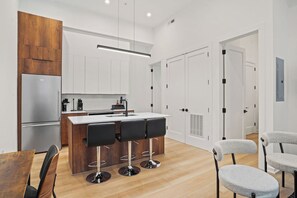 A modern kitchen with a central island, bar stools, a refrigerator, and white cabinetry. - Downtown DC Gem | Minutes to Convention Center (Washington)