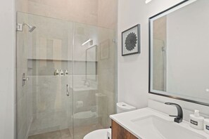 Un baño moderno con ducha de vidrio, un espejo grande y un lavabo blanco con dispensadores de jabón.
