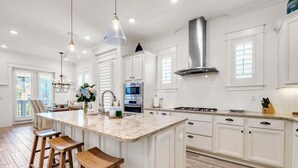 A spacious kitchen with white cabinetry, a large island with stools, stainless steel appliances, and pendant lighting. - 🦩Book Me Baby! Seaesta in Prominence🦩 (Inlet Beach)