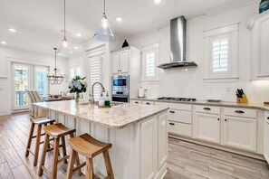 A spacious kitchen with white cabinetry, a large island with stools, stainless steel appliances, and pendant lighting. - 🦩Book Me Baby! Seaesta in Prominence🦩 (Inlet Beach)