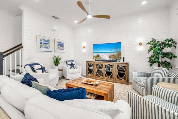 A living room with white walls, a ceiling fan, a large TV, and a wooden cabinet. - 🦩Book Me Baby! Seaesta in Prominence🦩 (Inlet Beach)