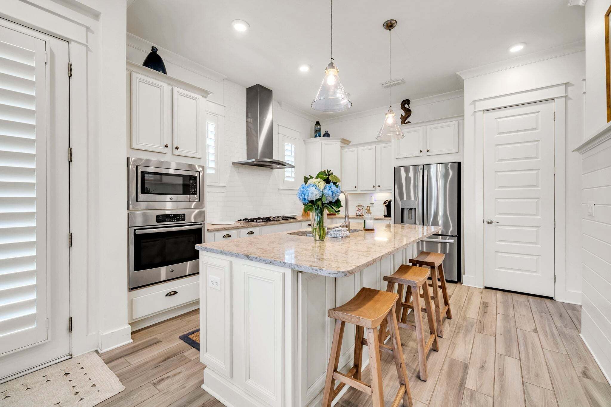 A kitchen with white cabinetry, stainless steel appliances, a marble island, wooden stools, and pendant lighting.