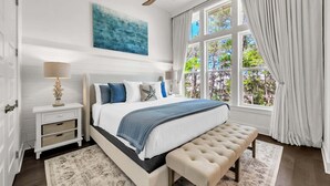A bedroom with a bed, bedside table, lamp, bench, and a view of trees through a window. - 🦩Book Me Baby! Seaesta in Prominence🦩 (Inlet Beach)