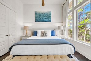 A bedroom with a large bed, a nightstand, a lamp, a painting, and a window with a view of trees. - 🦩Book Me Baby! Seaesta in Prominence🦩 (Inlet Beach)