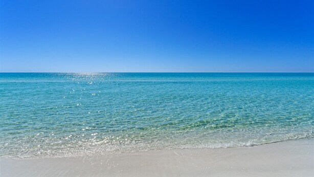 Una spiaggia con acqua cristallina dai riflessi turchesi e una battigia sabbiosa sotto un cielo azzurro intenso.