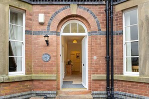 A brick building with a central arched doorway, a small porch, and a visible interior hallway. - Spacious Historic Home In Cockermouth With Parking (Cockermouth)