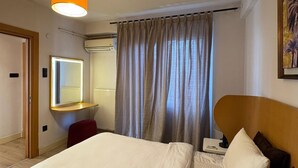 A hotel room with a bed, a desk with a chair, a mirror, an air conditioning unit, and a window with curtains. - Taksim Square-1br Rooftop Suite 07 (Istanbul)