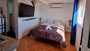 Ein Schlafzimmer mit einem Bett, einem an der Wand montierten Fernseher, einer Klimaanlage und einem Fenster mit Vorhängen.