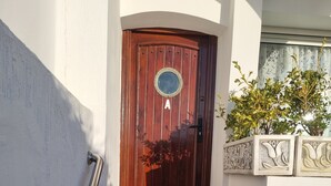 Eine Holztür mit rundem Fenster, einem Metallhandlauf und einer Treppe aus Stein, die zu einer weißen Wand mit dekorativen Verzierungen führt.