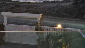 Blick auf die Küste mit einem Gewässer, einem weißen Zaun und einem Weg zu einem Gebäude.
