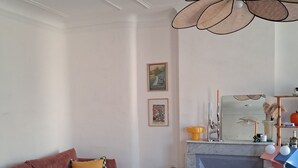 Un salon comprenant un canapé, une table basse en verre, un coin cuisine avec un évier et une cuisinière, et un luminaire suspendu.