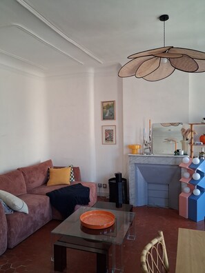 A living room with a sofa, a glass coffee table, a kitchen area with a sink and a stove, and a hanging light fixture. - Typical sunny apartment in Notre-Dame du Mont with balcony and air conditioning (Marseille)