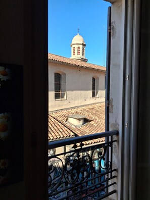 A view through a balcony railing of a building with a tiled roof, a dome-shaped tower, and a window with a metal grill. - Typical sunny apartment in Notre-Dame du Mont with balcony and air conditioning (Marseille)