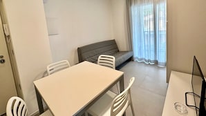 A small, well-lit room with a table and chairs, a sofa, and a window with curtains. - Apartment With Pool in Bibione (San Michele al Tagliamento)