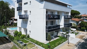 A modern multi-story building with balconies, a swimming pool, and a well-maintained garden. - Apartment With Pool in Bibione (San Michele al Tagliamento)