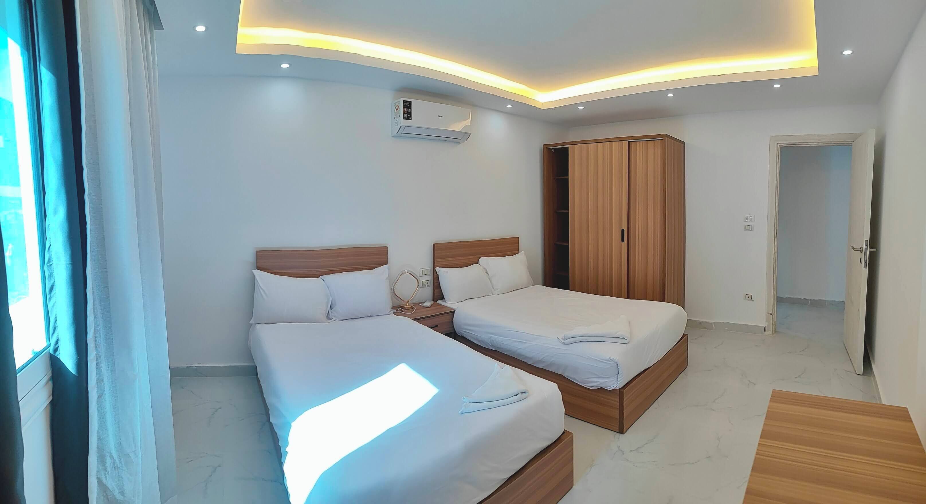 Ein Hotelzimmer mit zwei Betten, einem Kleiderschrank, einer Klimaanlage und einem Fenster mit Vorhängen.