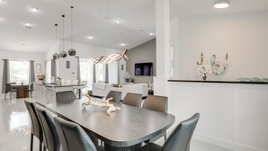 A modern kitchen with a central island, a dining area with a dark table and black chairs, and a living area with a sofa and TV. - Private Outdoor Oasis! Home 12 Mi to Flagler Beach (Palm Coast)