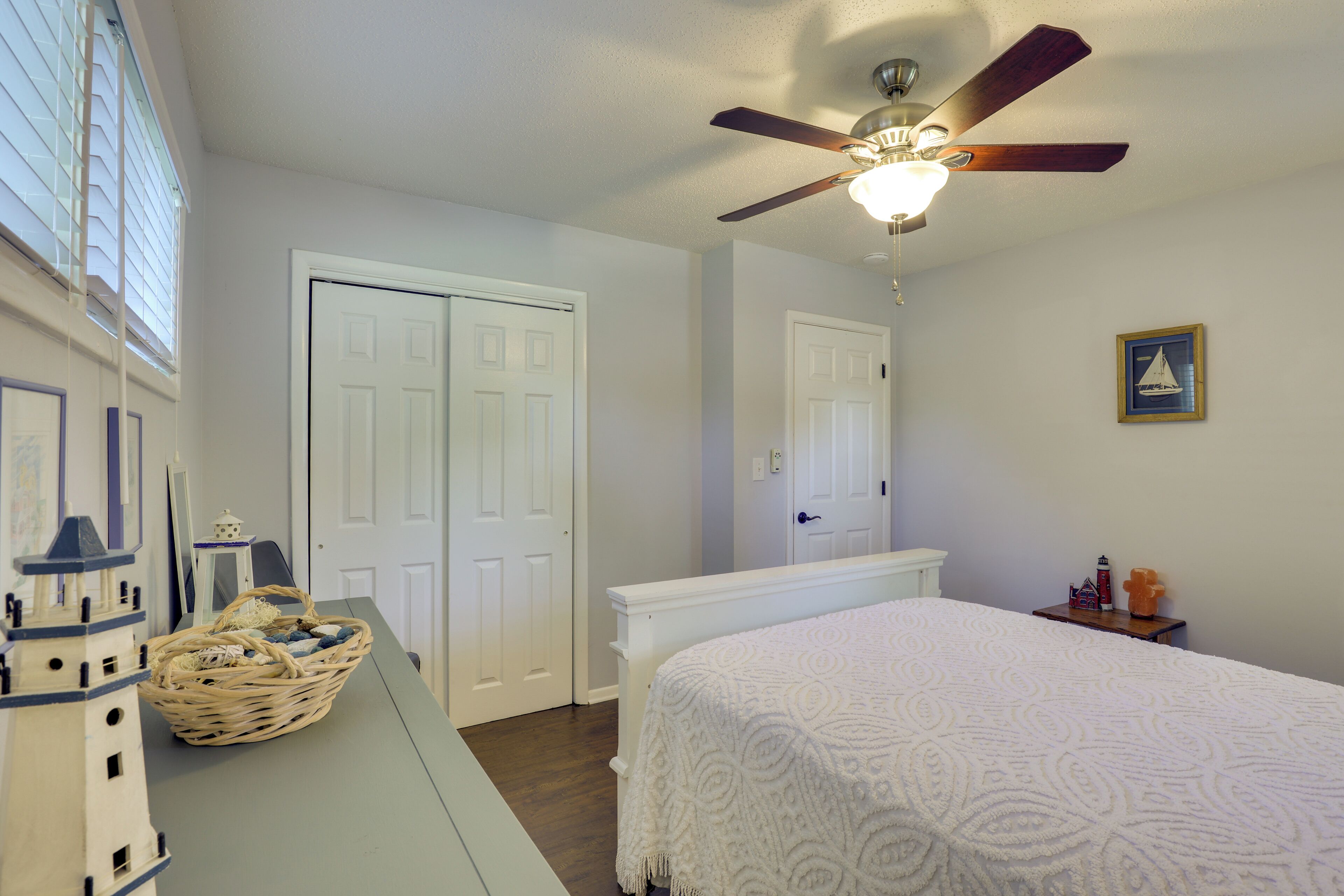 A bedroom with a bed, a ceiling fan, a window with blinds, and a wall-mounted picture.