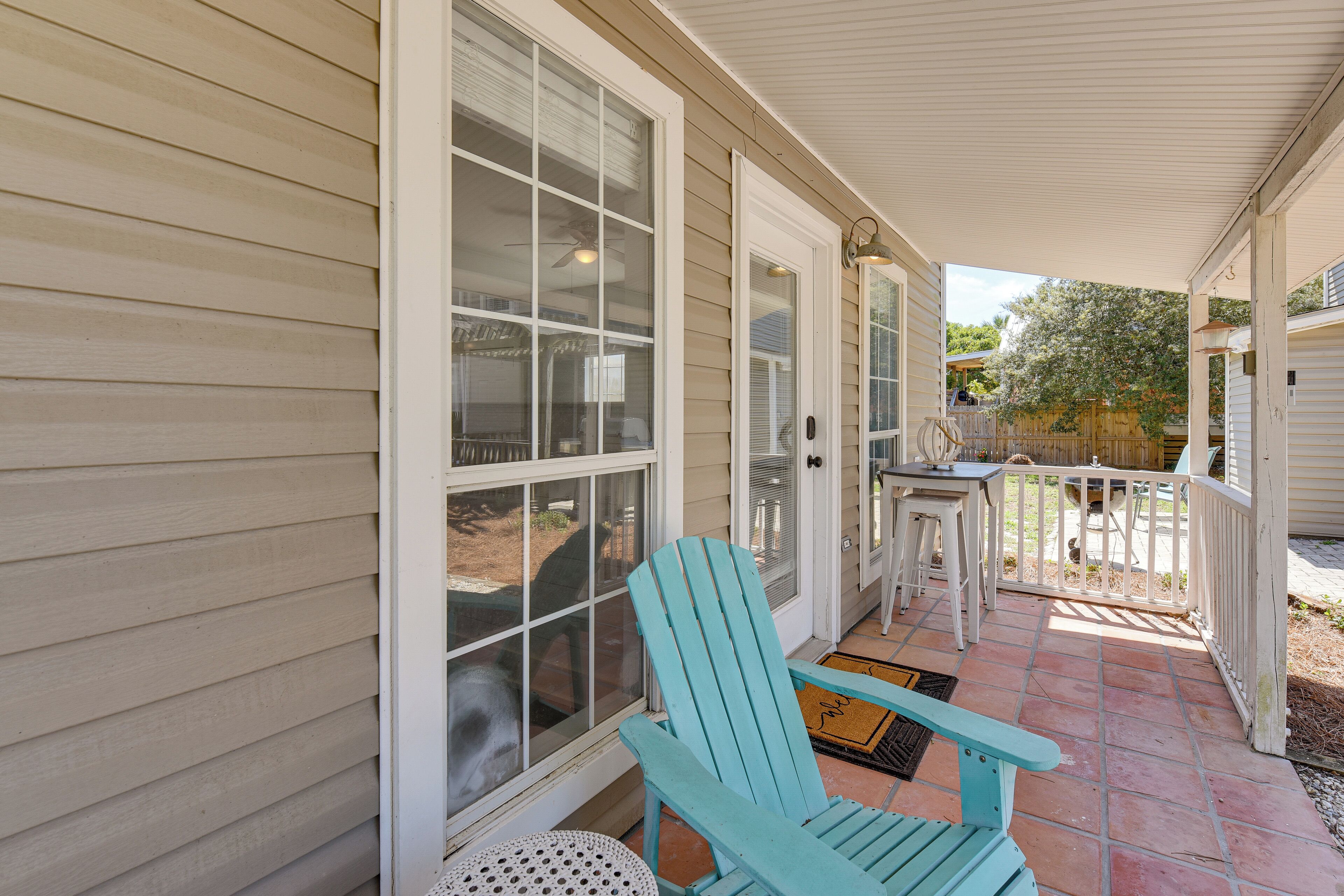 Eine überdachte Veranda mit blauem Adirondack-Sessel, einem kleinen Tisch und einer Tür mit Fenster.