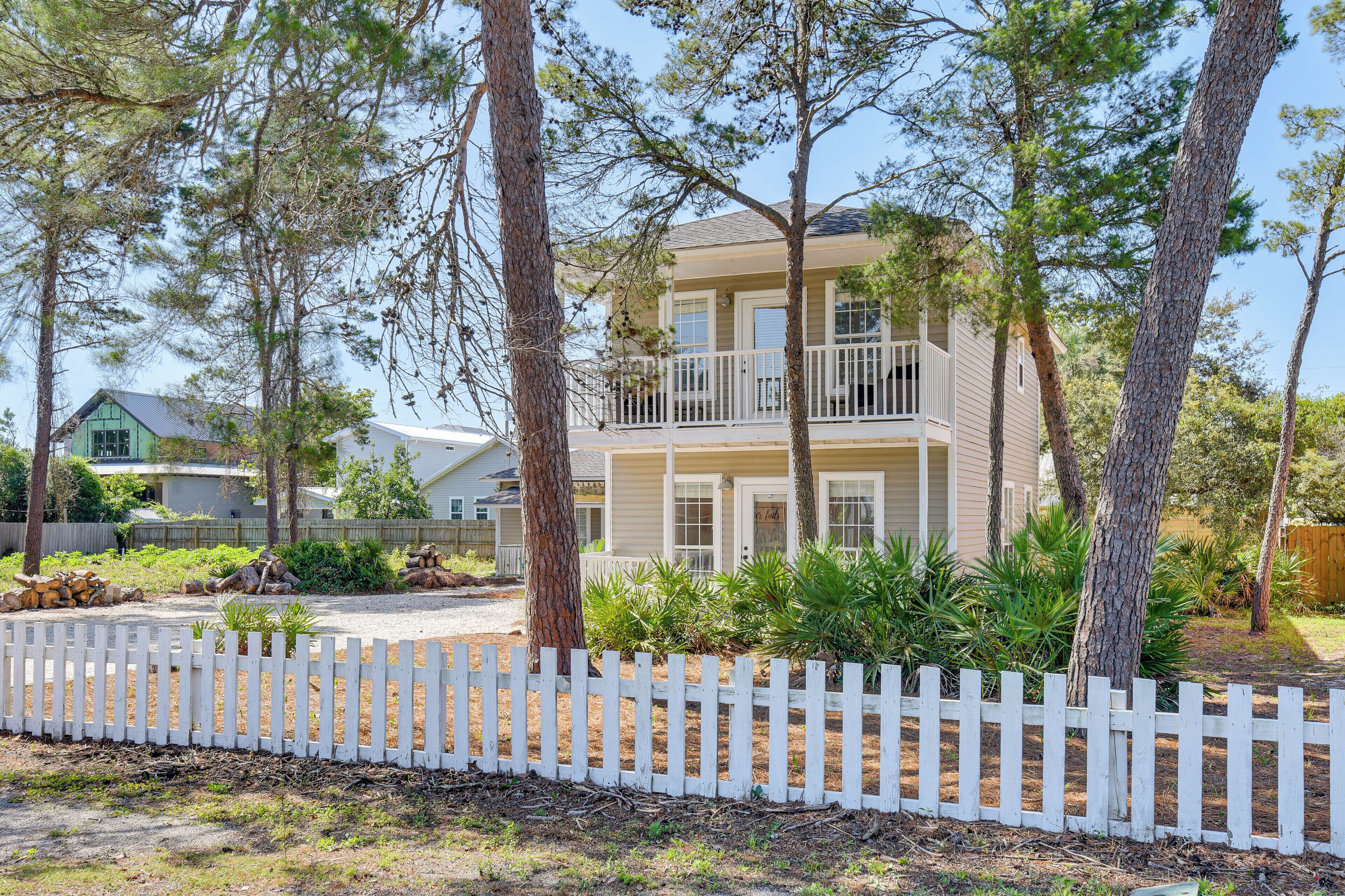 Ein zweistöckiges Haus mit Balkon, umgeben von Bäumen und einem weißen Zaun.
