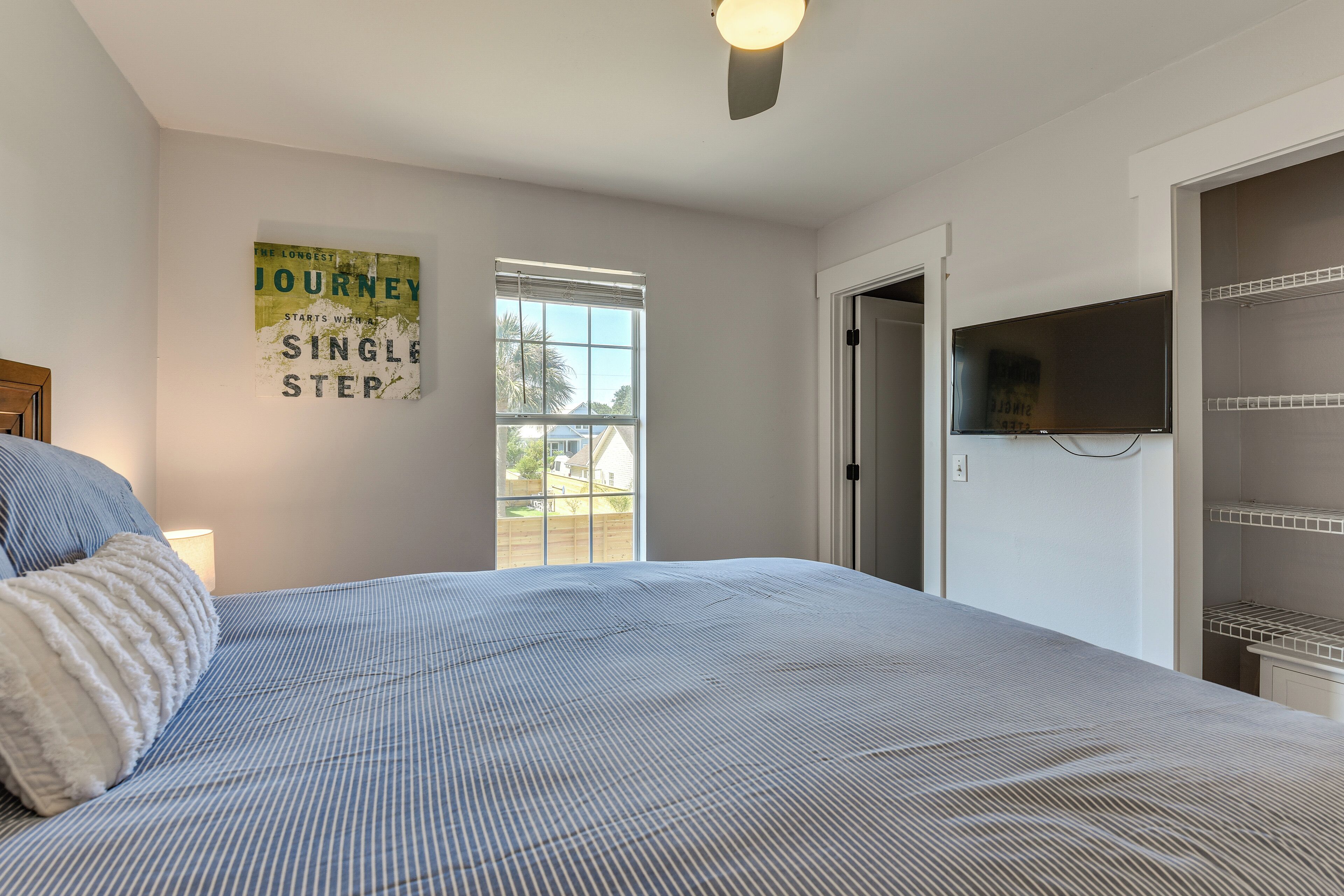 A bedroom with a bed, a wall-mounted TV, a window with blinds, and a door leading to a closet.