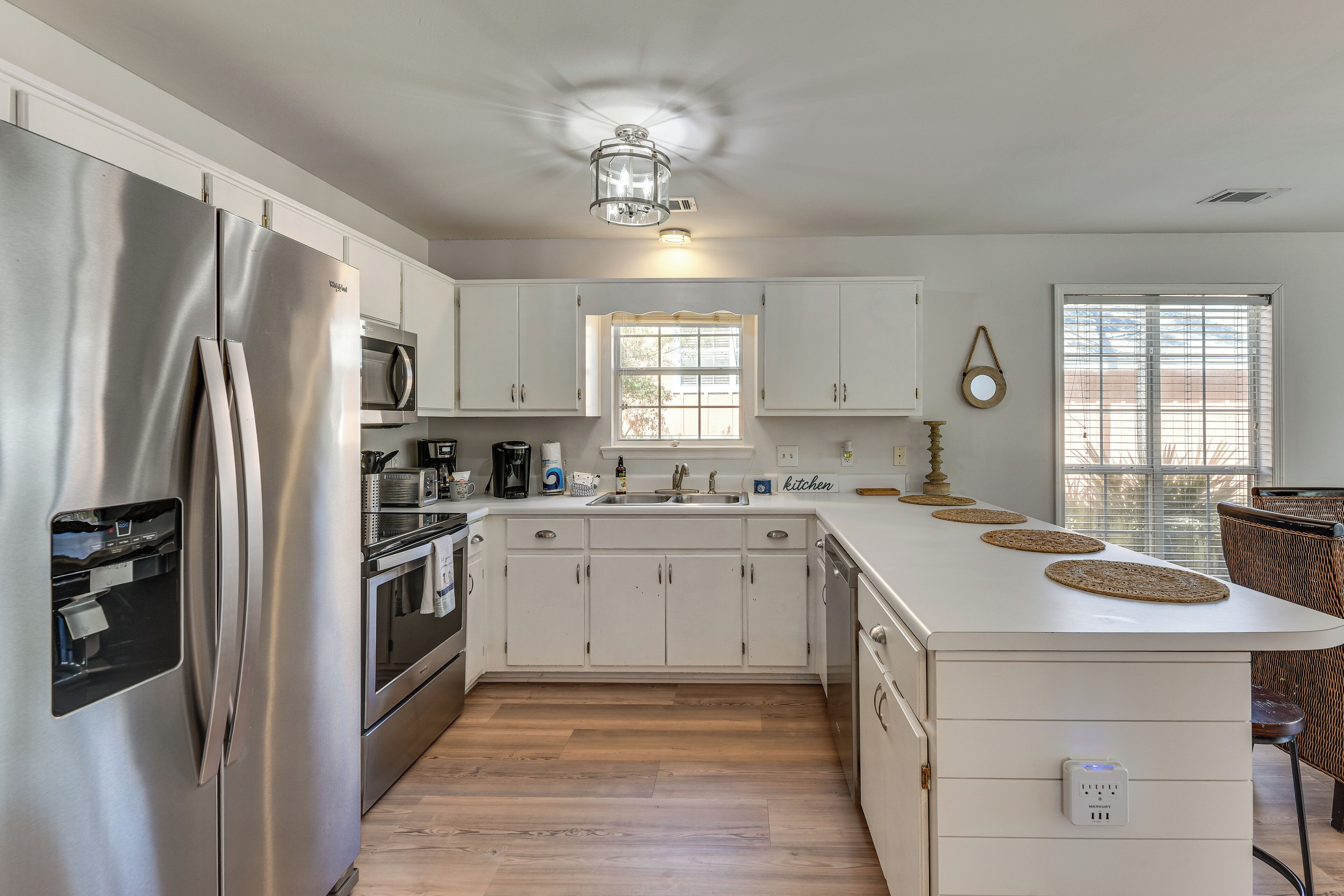 A modern kitchen with white cabinetry, stainless steel appliances, a central island, and a window providing natural light.