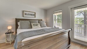 A bedroom with a wooden bed frame, a bedside table with a lamp, a framed sign on the wall, and a window with blinds. - Walk to Ocean & Eats: Santa Rosa Beach Cottage (Santa Rosa Beach)