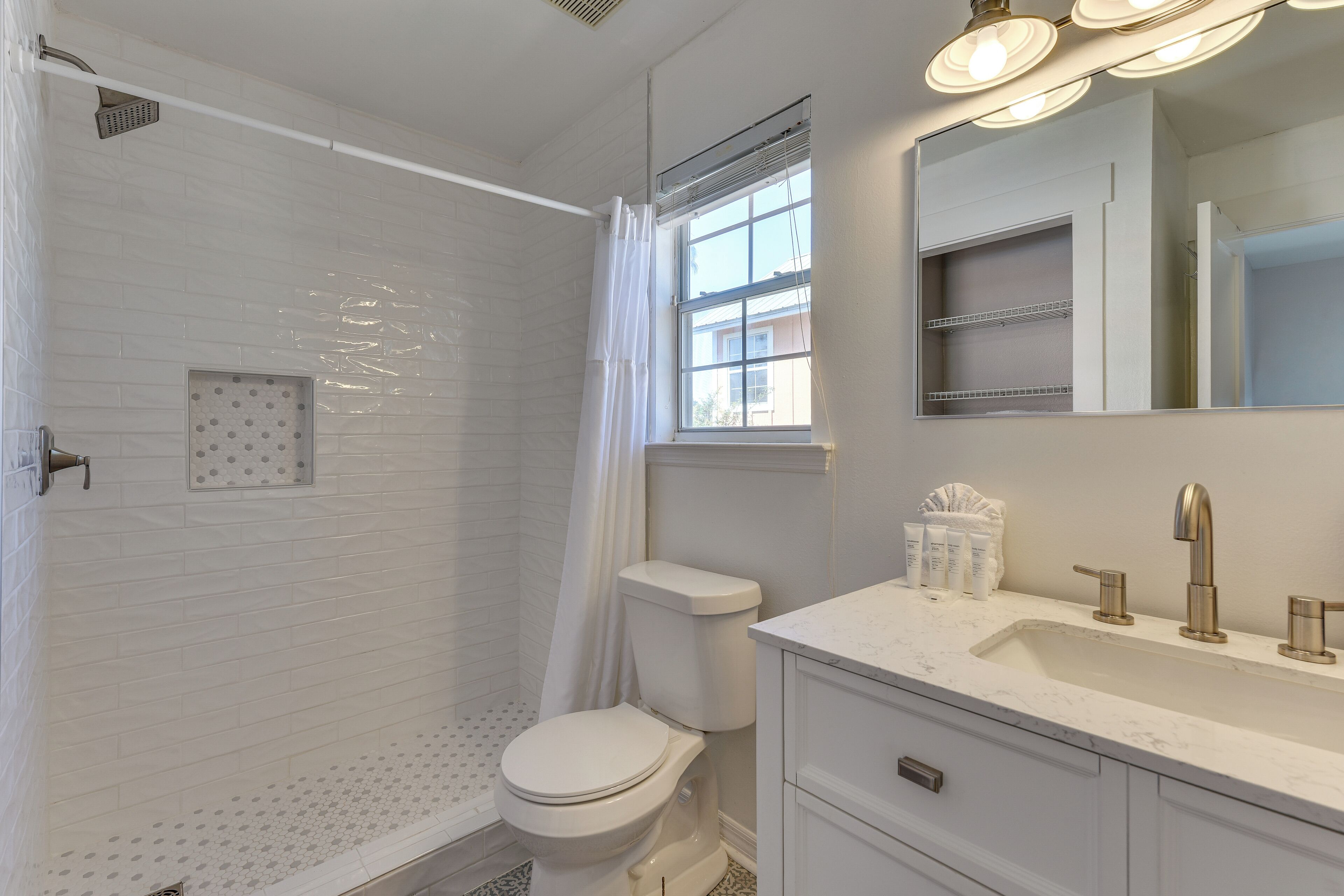 A bathroom with a shower, toilet, sink, and mirror.