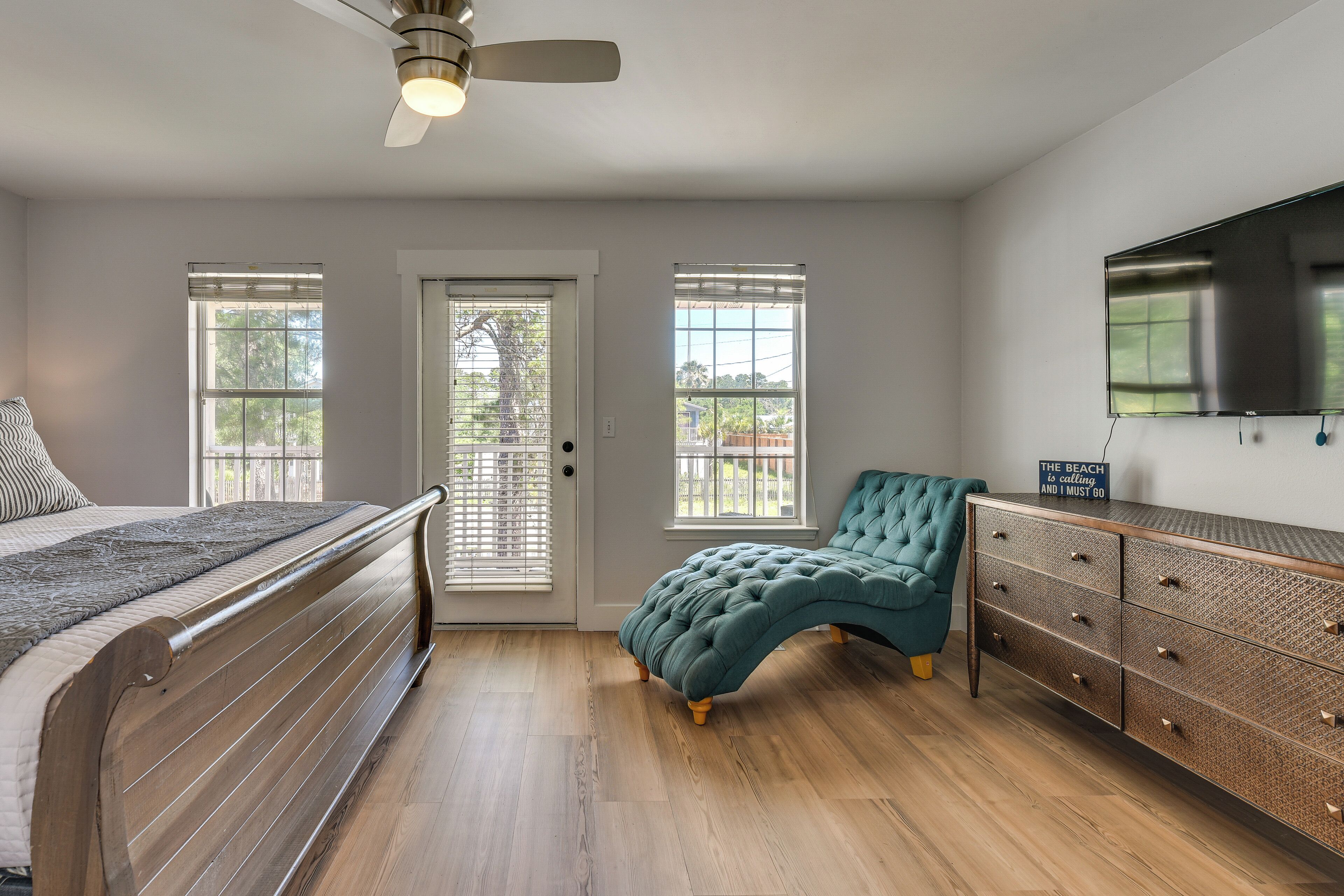 A bedroom with a bed, a dresser, a television, and a door with windows.