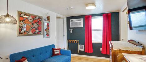 Una habitación con un sofá azul, un aparador de madera, una lámpara de techo y una ventana con cortinas rojas.